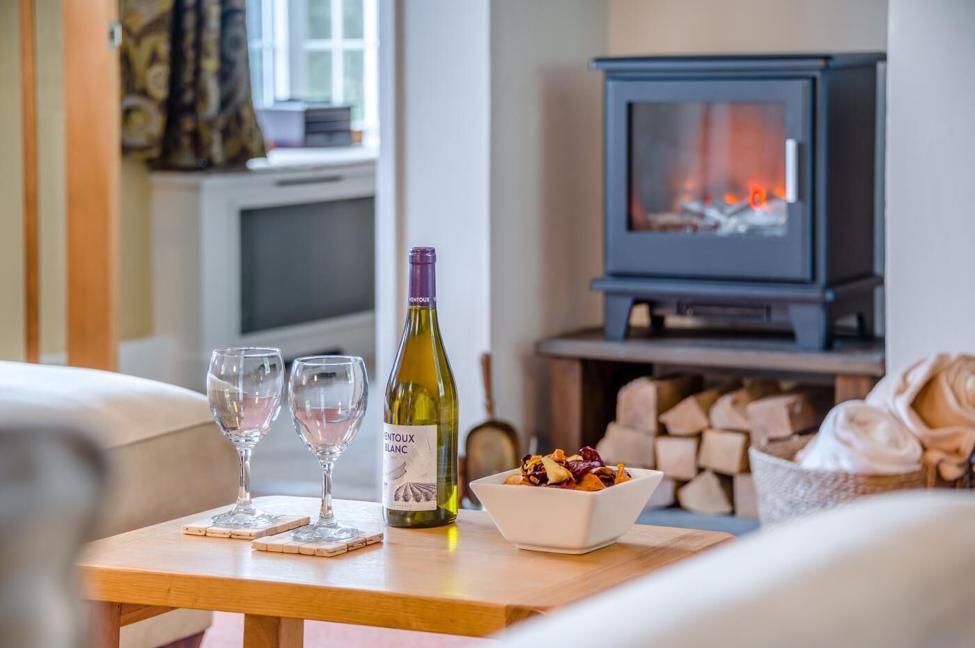 A cozy living room with a fireplace, a bottle of wine, and two glasses on a wooden table.