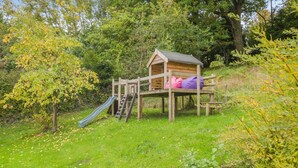 Une cabane en bois, dotée d’un toboggan et d’une échelle d’escalade, entourée d’une végétation luxuriante.