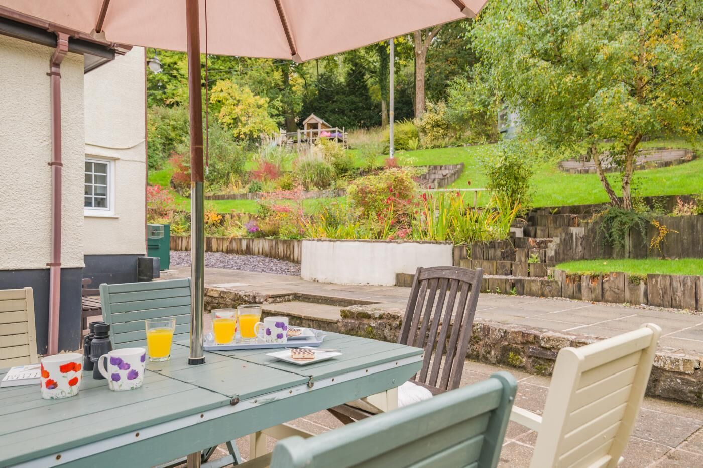 An outdoor patio with a table set for breakfast, surrounded by chairs, and an umbrella providing shade.