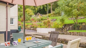 Une terrasse extérieure avec une table dressée pour le petit-déjeuner, entourée de chaises, et un parasol offrant de l’ombre.