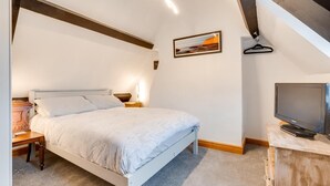 Ein Schlafzimmer mit Bett, Nachttisch, Lampe, Fernseher und einem Bild an der Wand.