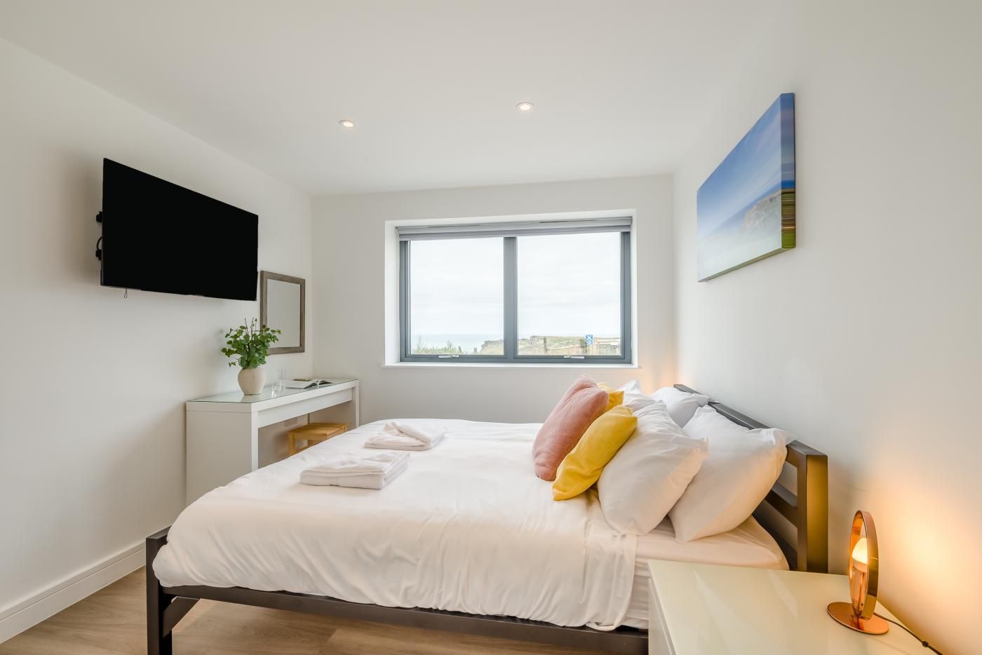 A hotel room with a bed, bedside table, lamp, window, and a flat-screen TV mounted on the wall.