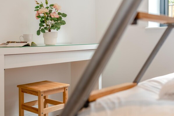 A room with a bed, a wooden stool, a white table with a potted plant, and a window. - 2 Bed in Tintagel (oc-p33627) (Tintagel)
