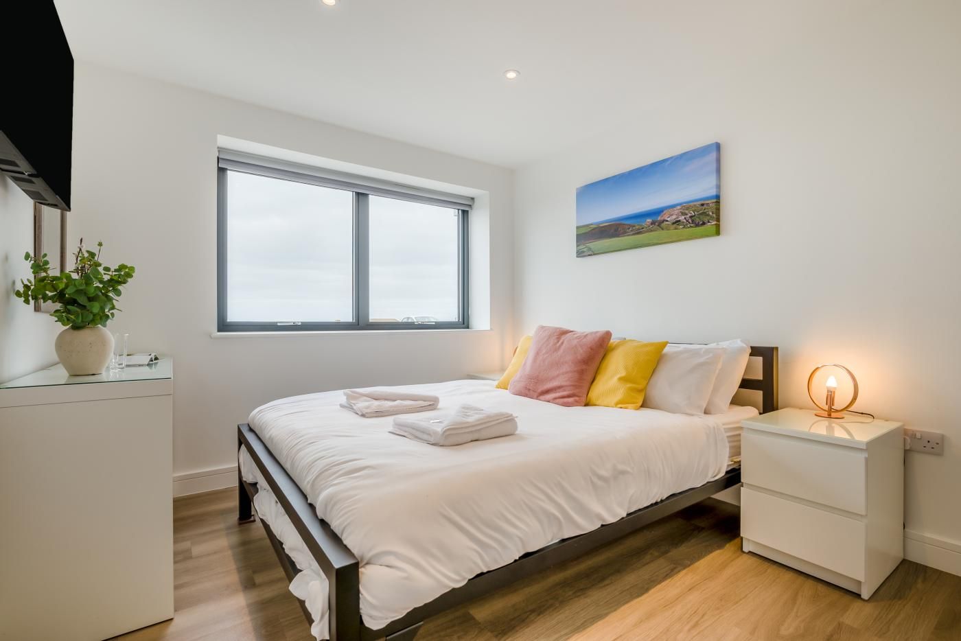 A bedroom with a bed, bedside tables, a nightstand, a window, and a painting on the wall.