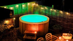 Ein Whirlpool, umgeben von Holzmöbeln und Lichterketten, vor einer Holzzaun.