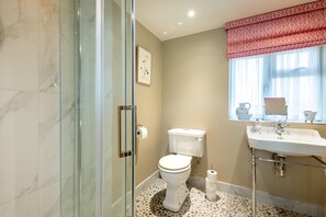 Et badeværelse med glasbrusekabine, toilet og vask med spejl over.