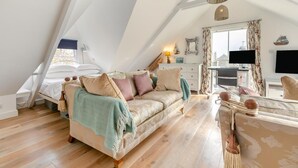 Ein gemütliches Schlafzimmer im Loft-Stil mit schrägem Dach, einem Bett, einer Couch und einem Schreibtischbereich mit Fernseher.