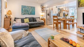 Ein modernes Wohnzimmer mit einer Couch, einem Esstisch und einer Küchenzeile mit Kühlschrank und Essplatz.