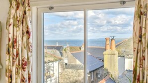 Ein Fenster mit Blick auf eine Küstenstadt, darunter Gebäude und ein Leuchtturm.