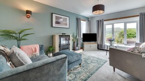 A modern living room with a fireplace, a flat-screen TV, and a large window offering a view of the outdoors. - 3 Bed in Askrigg (oc-ds1035) (Askrigg)