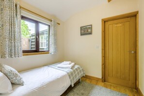 Een slaapkamer met een enkel bed, een raam met gordijnen, een houten deur en een klein schilderij aan de muur.