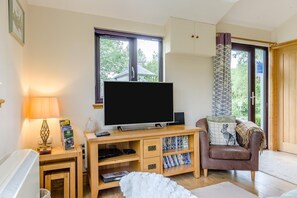A living room with a television, wooden entertainment unit, a brown leather sofa, and a window with a view of trees.