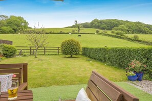 A grassy outdoor area with a wooden bench, a small table with a glass, and a potted plant. - 2 Bed in Brecon (oc-r33603) (Lower Chapel)