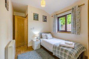 Une chambre à coucher comprenant un lit, une table de chevet, une lampe, une fenêtre avec des rideaux et un radiateur.