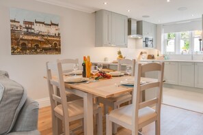 A dining area with a table set for four, a kitchen in the background, and a painting on the wall. - 3 Bed in Helmsley (oc-y111) (Helmsley)