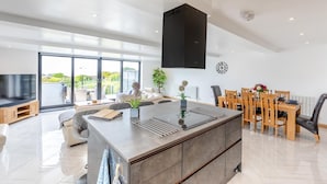Una cocina moderna con una isla central, zona de comedor con sillas de madera y un amplio ventanal que ofrece vistas al exterior.