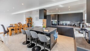 Una cocina moderna con armarios oscuros, una isla central con taburetes y una zona de comedor con mobiliario de madera.