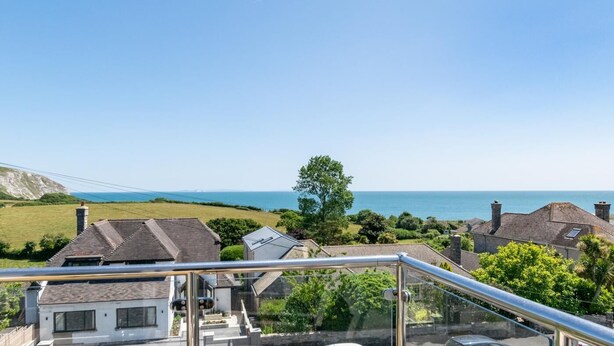 A coastal residential area with houses, a clear sky, and a view of the sea. - 4 Bed in Swanage (oc-wy617) (Swanage)