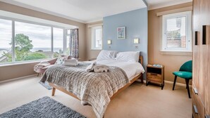 A bedroom with a large bed, a bedside table, a chair, and a view of the outdoors. - 4 Bed in Swanage (oc-wy617) (Swanage)