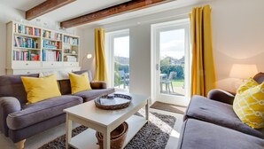 A living room with a sofa, a coffee table, a bookshelf, and a view through a glass door. - 3 Bed in Beadnell (oc-566714) (Swinhoe)
