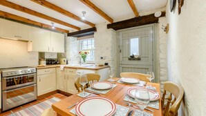 A kitchen with wooden beams, a stove, cabinets, and a dining table set for four with plates and glasses. - 2 Bed in St Davids (oc-30269) (St Davids)