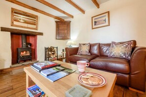 A cozy living room with a leather sofa, a wooden coffee table with books and a mug, a fireplace, and a wooden ceiling. - 2 Bed in St Davids (oc-30269) (St Davids)