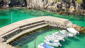 A marina with boats docked at a curved concrete pier surrounded by clear turquoise water and rocky cliffs. - 2 Bed in St Davids (oc-30269) (St Davids)