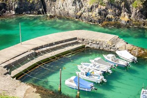 Ein Yachthafen mit Booten, die an einer gebogenen Betonpier liegen, umgeben von klarem türkisblauem Wasser und felsigen Klippen.