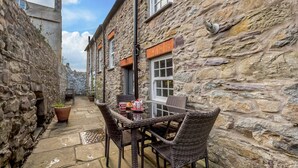 A narrow stone alley with a wicker table set for two, a potted plant, and a window with shutters. - 2 Bed in St Davids (oc-30269) (St Davids)