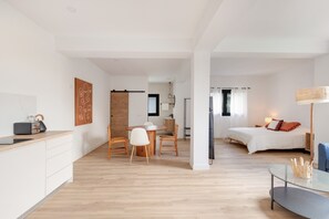 Una habitación de hotel moderna con cama, escritorio, silla, mesa de comedor y zona de cocina.