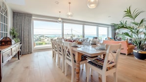 A spacious dining area with a large table, white chairs, and pendant lights. - 5 Bed in Polzeath (oc-r33648) (Polzeath)