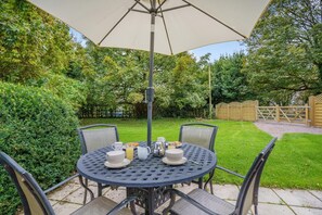Une table ronde d’extérieur avec des chaises, un parasol et des aliments pour le petit-déjeuner.