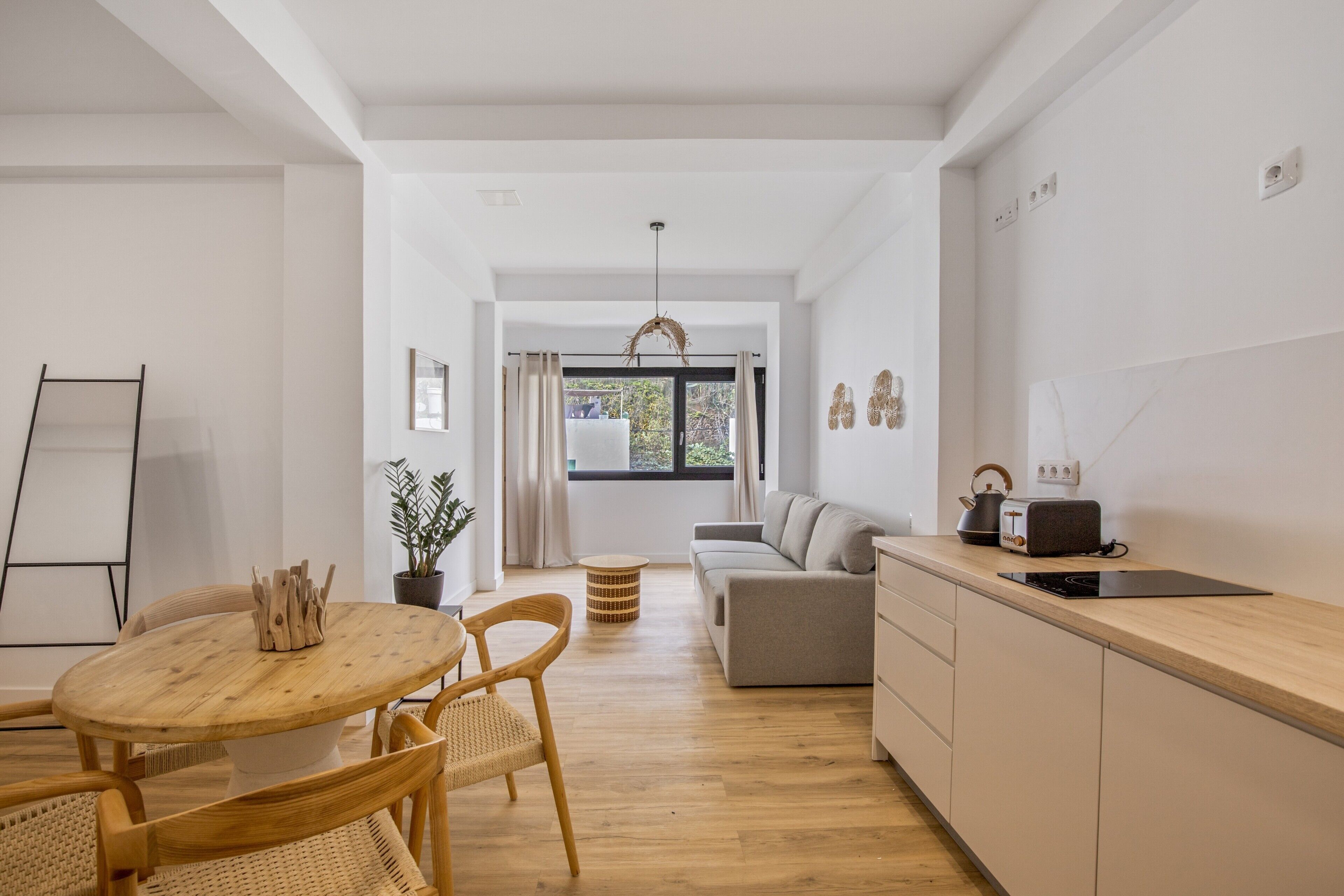 Un espai de vida modern amb zona de menjador, cuina i vista per una finestra gran.