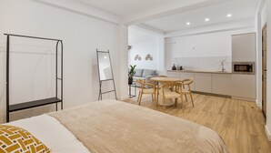 Et moderne hotelværelse med seng, skrivebord, stol, et lille tekøkken og en whiteboard.