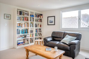 A living room with a leather sofa, a wooden coffee table, a bookshelf, and a window with a view of buildings.