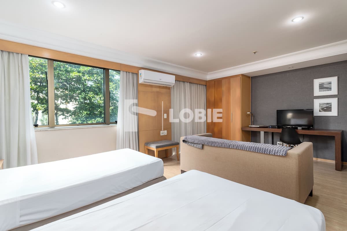 Quarto de hotel moderno com duas camas, um sofá, uma TV e uma escrivaninha.
