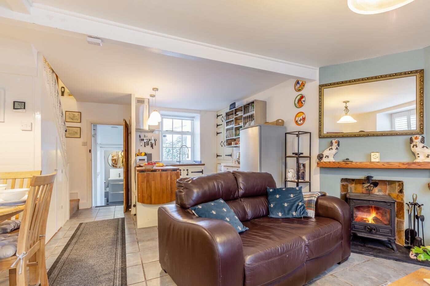 A cozy living room with a brown leather sofa, a fireplace, and a kitchen in the background.