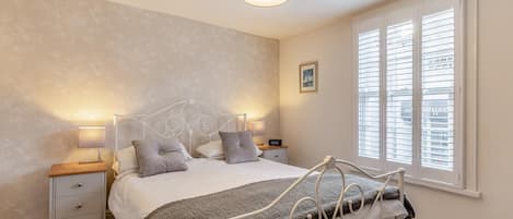 A bedroom with a bed, bedside lamps, a nightstand, a window with blinds, and a ceiling light fixture.