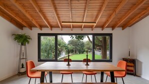 A dining area with a wooden table and four chairs, large windows with a view of greenery, and a tall floor lamp. - Vacation Apartment '6' with Mountain View, Shared Terrace and Garden (Moya)