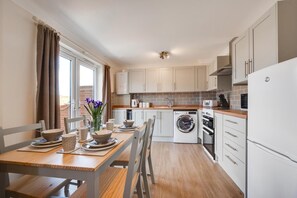 Una cucina moderna con zona pranzo, completa di lavatrice, forno e mobili bianchi.