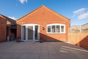 A brick building with a white door and windows, a paved courtyard, and a wooden fence. - 3 Bed in Chedgrave (oc-2252) (Chedgrave)