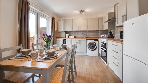 A modern kitchen with a dining area, white cabinets, a washing machine, and a refrigerator. - 3 Bed in Chedgrave (oc-2252) (Chedgrave)