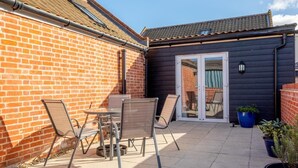 A patio with a table and chairs, a blue planter, and a brick wall. - 3 Bed in Chedgrave (oc-2252) (Chedgrave)