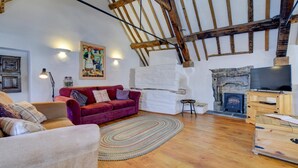 A cozy living room with a red sofa, wooden beams, a stone fireplace, and a television on a wooden stand. - 2 Bed in Machynlleth (oc-197758) (Machynlleth)