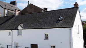 A white building with a steeply pitched roof, multiple windows, and a visible chimney. - 2 Bed in Machynlleth (oc-197758) (Machynlleth)