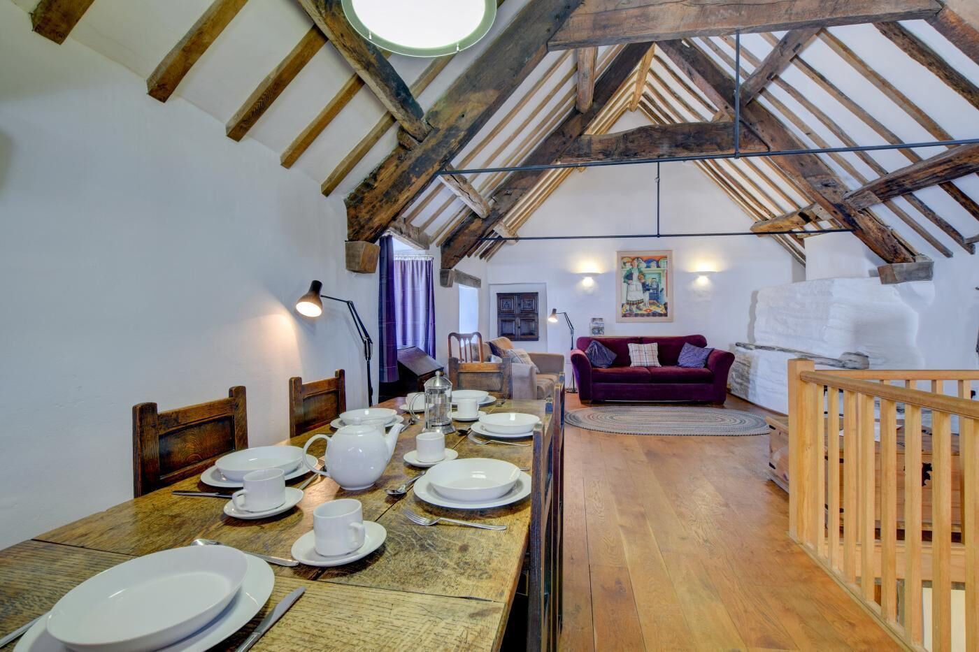 A dining area with a wooden table set for a meal, a sofa, and a wooden railing.