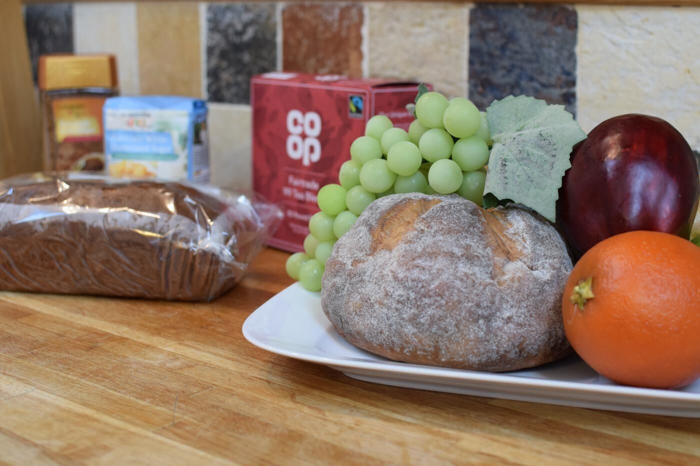 Een bord met brood, druiven, een aubergine en een sinaasappel op een houten tafel.