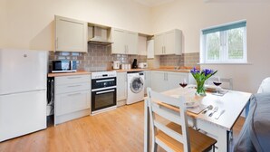 A modern kitchen with white cabinetry, a built-in oven, microwave, and washing machine. There's a dining table with chairs and a window with a view.