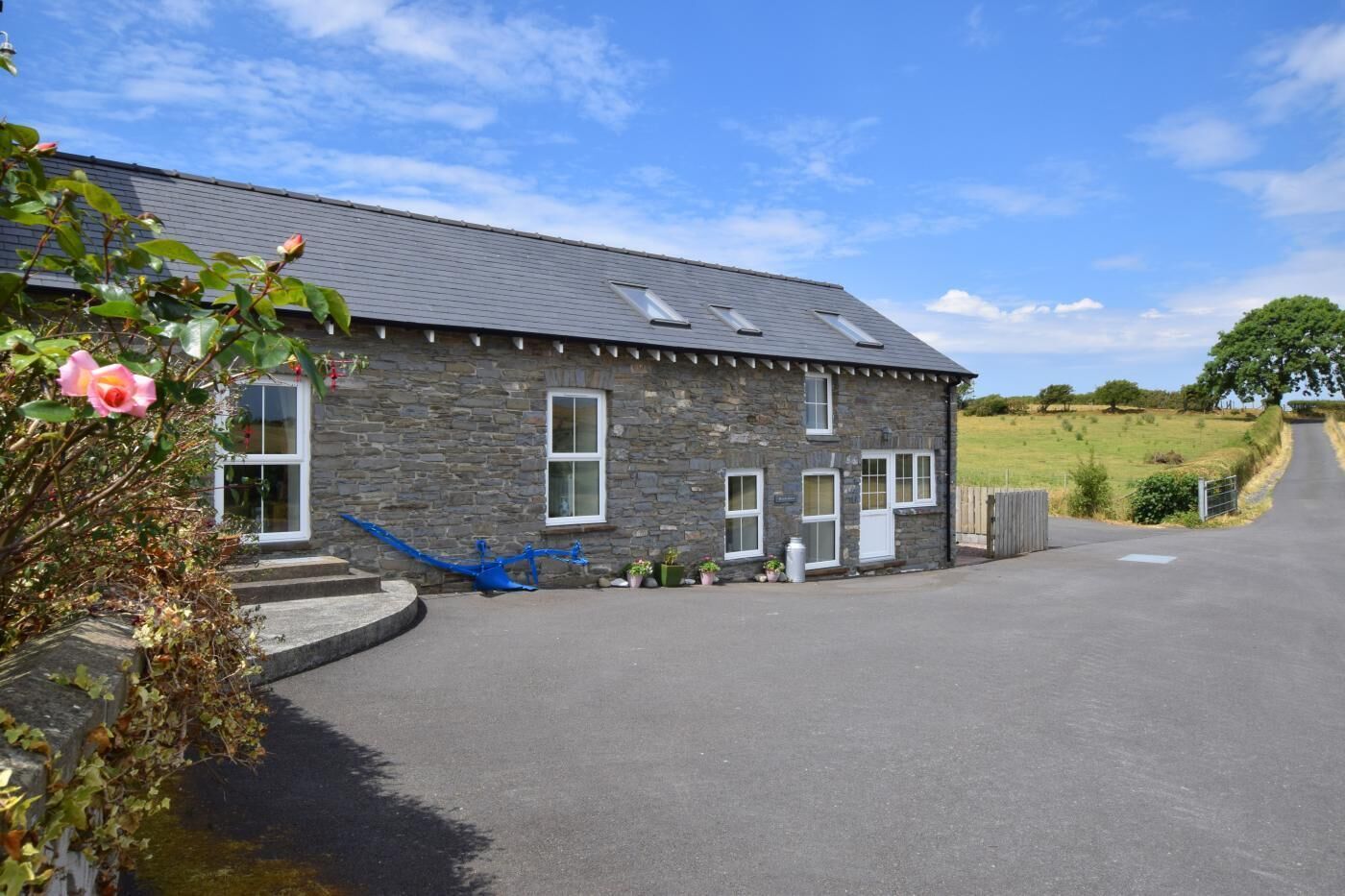 A stone building with a sloped roof, a driveway, and a rural landscape.