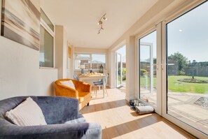 A modern living room with a sofa, a dining area with a table and chairs, and a large sliding glass door leading to a backyard. - 2 Bed in Heacham (oc-2263) (Heacham)